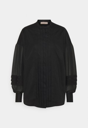 Chemise noire avec col montant, devant plissé et manches bouffantes transparentes avec accents de tissu superposés. Texture lisse et design classique.