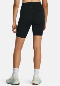 Shorts da ciclismo neri a vita alta con una consistenza liscia. Presentano un design aderente e cuciture minimaliste. Abbinati a scarpe da ginnastica di colore chiaro.