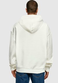 Cremefarbener Kapuzenpullover, Oversized-Schnitt, weicher Stoff, Kapuze mit Kordelzug, gerippte Bündchen und Saum sowie nahtloses Schulterdesign, kombiniert mit blauen Jeans.