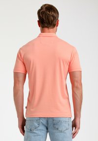 Kortärmad polo t-shirt i korallfärg, tillverkad av mjukt tyg. Har en krage och en modern passform, i kombination med ljusa denimjeans.