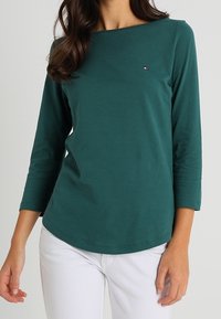 Groene lange mouw top met een ronde hals, gemaakt van zachte stof. Heeft een klein logo op de borst en een gebogen zoom.