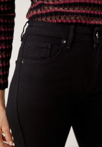 Černé džínové kalhoty se klasickým střihem, s malou přední kapsou, viditelným švem a standardním zapínáním na knoflík a zip.