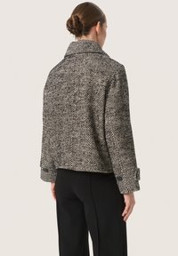 Zwart-wit houndstooth-gestreepte jasje met een brede kraag, cropped ontwerp en met knopen gesloten mouwen, gemaakt van gestructureerde stof.