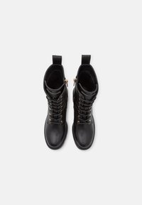 Czarne skórzane botki za kostkę z ozdobnymi złotymi oczkami i suwakiem z boku, widok z góry na białym tle.