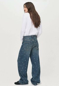 Blue denim wide-leg jeans with embroidered circular patterns. Features a standard waistband and five-pocket design.