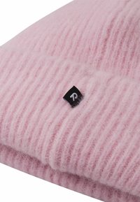 Jasnoróżowa wełniana czapka z miękkiego materiału, z pionowym prążkowaniem i małą czarną metką z białym logo.