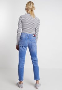 Světlé modré džíny s vysokým pasem, zúženými nohavicemi a dvěma zadními kapsami. Obsahují značkovou nášivku na pase. Pruhované tričko s dlouhým rukávem.