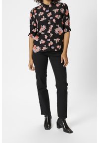 Czarna bluzka w kwiatowy nadruk w kolorze różowym i niebieskim, krótki rękaw z falbanami, zapinana na guziki z przodu, noszona z czarnymi spodniami o dopasowanym kroju i botkami za kostkę.