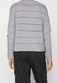 Light gray knit sweater featuring horizontal stripes with open weave details. Rounded neckline and long sleeves. Rounded hem at the back.
