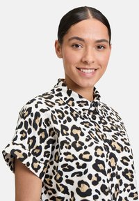 Leopard print shirt made of lightweight fabric. Features short sleeves, a button-up design, and black and tan animal patterns on a white background.