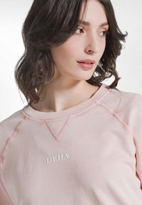 Sudadera rosa claro con cuello redondo, que presenta un detalle de puntada texturizada y el logo "DEHA" bordado en blanco en el frente.