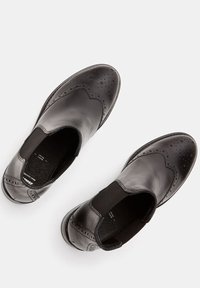 Czarne skórzane buty z elastycznymi bokami, zaokrąglonym noskiem oraz perforowanymi detalami wzdłuż szwów. Płaska podeszwa i teksturowana podszewka wewnętrzna.