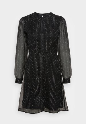 Sort kjole med knaplukning, gennemsigtige lange ærmer, dekoreret med hvide polkaprikket og lodrette striber, samt en figursyet talje.