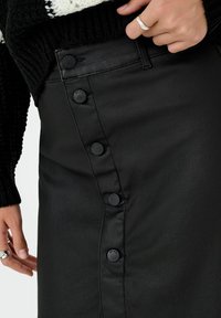 Zwarte kokerrok van faux leer met een zijknopsluiting met zes zwarte knopen, een gladde textuur en minimale stiksels.