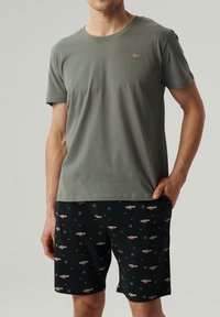 Oliwkowy bawełniany T-shirt z okrągłym dekoltem, w zestawie z czarnymi szortami zdobionymi kolorowymi napisami i wzorami logo.