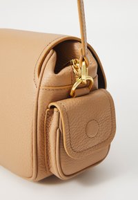 Camel-colored leather handbag with a rounded shape, featuring a small front pocket and gold hardware accent. Textured surface detail.