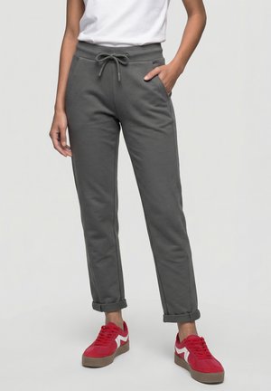 Person wearing gray drawstring pants with rolled cuffs, white shirt, and red sneakers with white accents, standing with one hand in pocket.