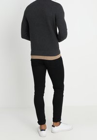 Donkergrijs geribbeld trui met een beige zoom, gecombineerd met zwarte slim-fit broek en witte sneakers met navy accenten.