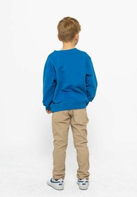 Blå crewneck sweatshirt, beige byxor och vita sneakers, sedd bakifrån. Sweatshirten har en avslappnad passform med ribbade ärmslut och nederkant.