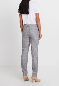 Szare spodnie w kratę o dopasowanym kroju, z delikatną teksturą i smukłym sylwetką. Noszone z białym t-shirtem i cielistymi szpilkami.