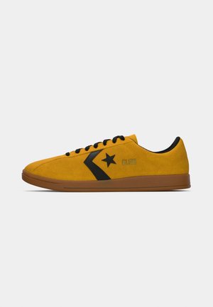 Lavtop sennepsgul ruskinds sneaker med sort stjerne logo, sorte snørebånd og brun sål, set fra siden på en hvid baggrund.