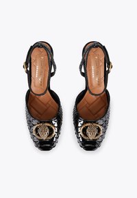 Czarne lakierowane szpilki slingback z teksturowaną powierzchnią, detal z okrągłego złotego sprzętu oraz pikowaną beżową wkładką.