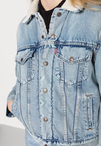 Lichtblauwe denimjacket met een kraag van fauxbont, zilveren knopen, twee borstzakken en stikdetails. Zachte textuur met een relaxte pasvorm.