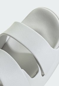 Valkoiset liukusandaalit, joissa on teksturoidut, leveät hihnat. Suunniteltu avoimella varpaalla ja hieman muotoillulla pohjallisella mukavuuden takaamiseksi. Sileä viimeistely.