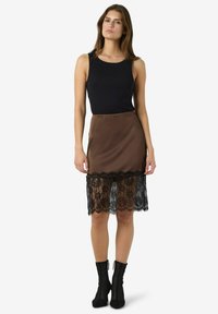 Svart ermeløs topp kombinert med en brun satengskjørt med blondetrim ved falden. Skjørtet har en glatt tekstur og en tettsittende passform.