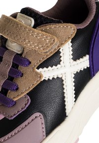 Sneaker in pelle nera con accenti viola, pannello in suede beige, cuciture bianche a croce e suola in gomma testurizzata. Strappo in velcro e lacci viola.