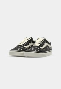 Black low-top sneakers with white laces and soles, decorated with small white and yellow daisy patterns.