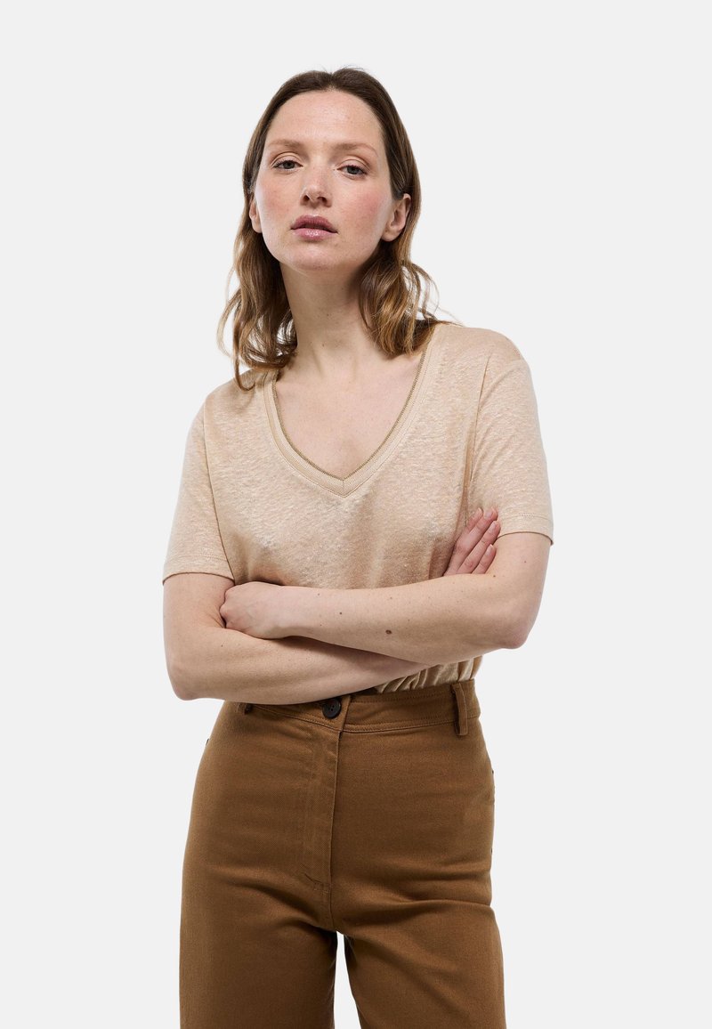 Haut beige à col en V et manches courtes en matériau léger, avec une texture subtile. Associe avec un pantalon marron taille haute.