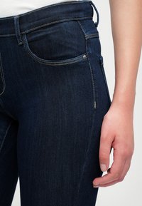 Mørkeblå denimjeans med en tettsittende design, med en jevn tekstur, klassisk fem-lommers stil og kontraststingdetaljer.