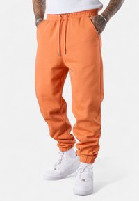 Orange Sweatpants mit elastischem Bund, Kordelzug und gestrickten Knöcheln. Weicher Stoff, Seitentaschen und ein dezenter, geprägter Logo-Detail.