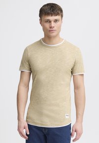 Tricou cu mânecă scurtă și guler rotund, fabricat dintr-un material ușor. Culoare texturată aurie cu accente albe la guler și la mâneci. Etichetă pe tiv.