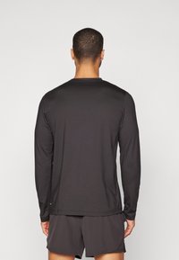 Černé tričko s dlouhým rukávem z hladké, lehké látky, s kulatým výstřihem a volným střihem, v kombinaci s odpovídajícími kraťasy.