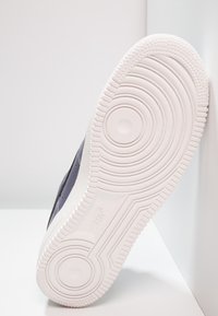 Ciemnoniebieski sneaker z teksturowaną powierzchnią i białą gumową podeszwą, z okrągłymi wzorami bieżnika i detalem logo Nike po boku.