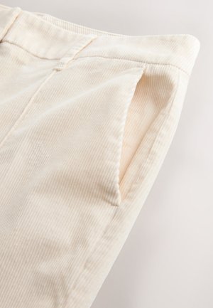 Pantaloni din corduroy crem deschis cu nervuri verticale și buzunare laterale, evidențiind o textură moale și detalii curate de cusături.