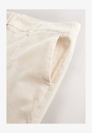 Helle Cremesamtcord-Hose mit vertikalen Rippungen und Seitentaschen, die eine weiche Textur und saubere Nahtdetails zeigen.