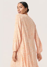 Långärmad klänning med orange och vit blommönstring i lätt material, som har en avslappnad passform och veckad detaljer vid axlarna.