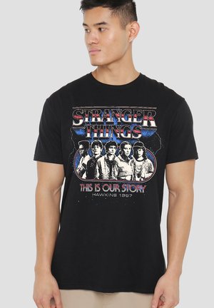 Schwarzes Baumwoll-T-Shirt mit einem Grafikdruck von fünf Figuren aus "Stranger Things" und dem Text „DAS IST UNSERE GESCHICHTE“ sowie "HAWKINS 1987".