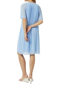 Helles blaues plissiertes Kleid mit kurzen Ärmeln, einem runden Ausschnitt und einem mittellangen Saum. Getragen mit weißen Wedgesandalen.