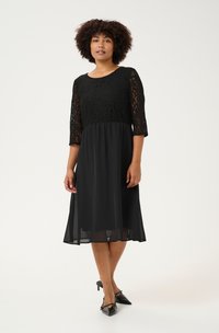 Rochie neagră cu corset din dantelă, mâneci trei sferturi și fustă fluidă. Finisaj satin, până la genunchi, cu o siluetă evazată.