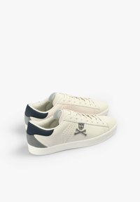 Beige leather sneakers with navy accents, featuring a skull and crossbones design, and textured gray heel patch. Laced design.