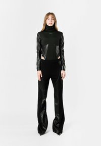 Top negro de manga larga con tejido brillante y detalles con corte, combinado con pantalones negros a medida con acentos de cuero y dobladillos afilados.
