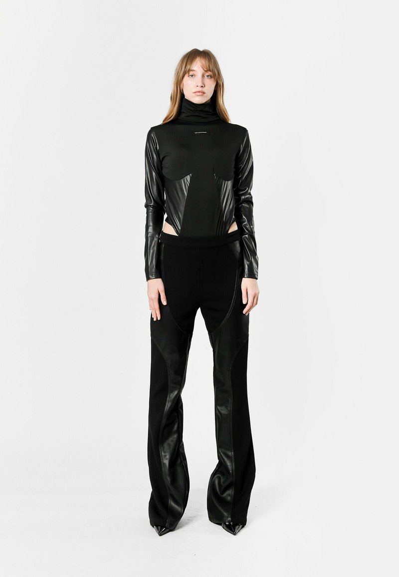 Top negro de manga larga con tejido brillante y detalles con corte, combinado con pantalones negros a medida con acentos de cuero y dobladillos afilados.