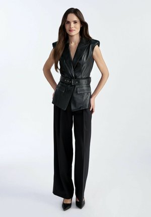 Czarna skórzana kamizelka z poduszkami na ramionach, z paskiem w talii i dwiema przednimi kieszeniami, w połączeniu z czarnymi spodniami o szerokich nogawkach i czółenkami z zakrytymi palcami.