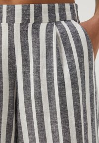 Pantalons en lin rayés gris et blanc avec une coupe décontractée, des plis à la taille et des poches latérales pour plus de fonctionnalité.