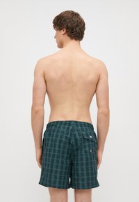 Calções de banho em verde-azulado escuro com padrão quadriculado. Apresentam uma cintura elástica e um bolso traseiro com fecho de botão.