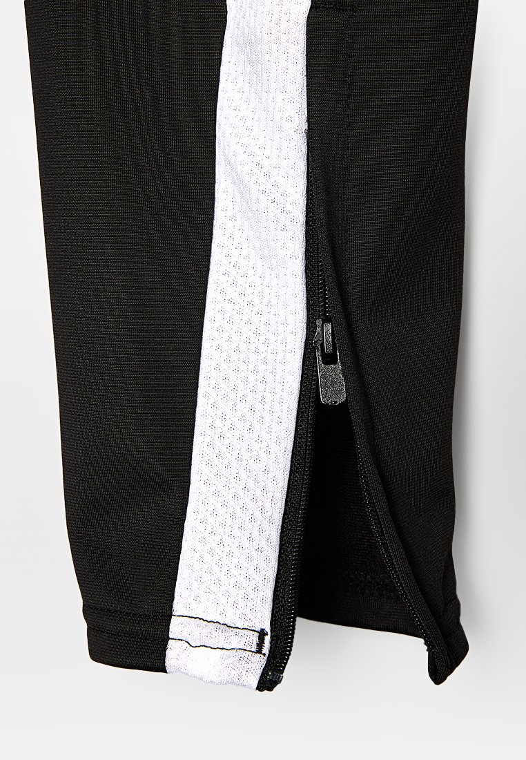 Czarne spodnie sportowe z bocznym zamkiem. Biała siateczkowa aplikacja na boku z teksturowanym materiałem. Widoczne szwy i gładkie elementy zamka.